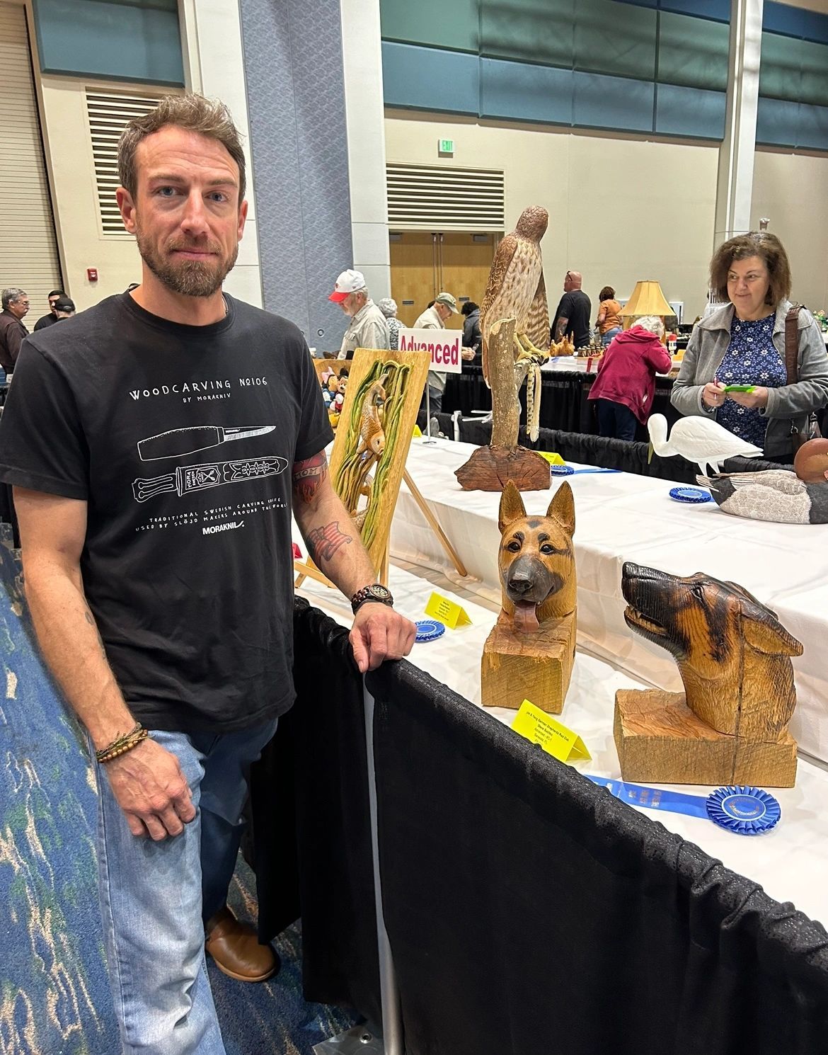 Steve Sushko standing beside his carved German shepherd busts at a wood carving show