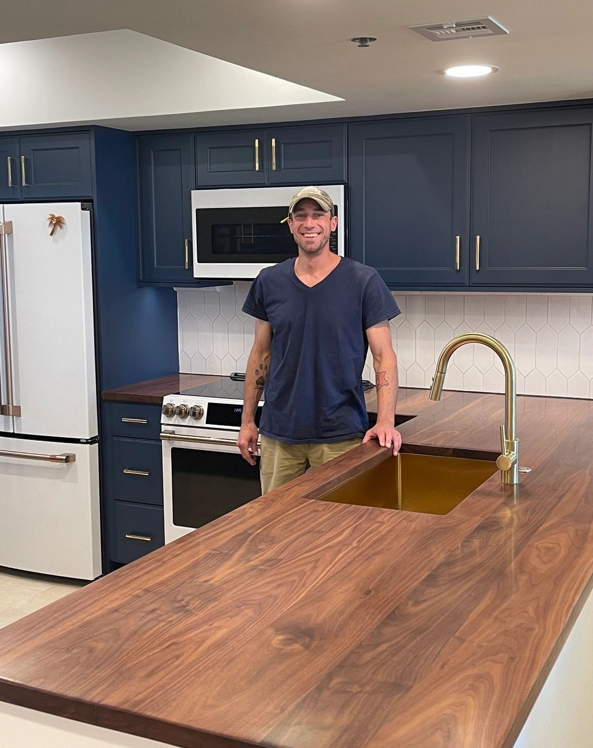 Steve Sushko standing at a walnut kitchen island he built, with a brass sink and navy cabinets